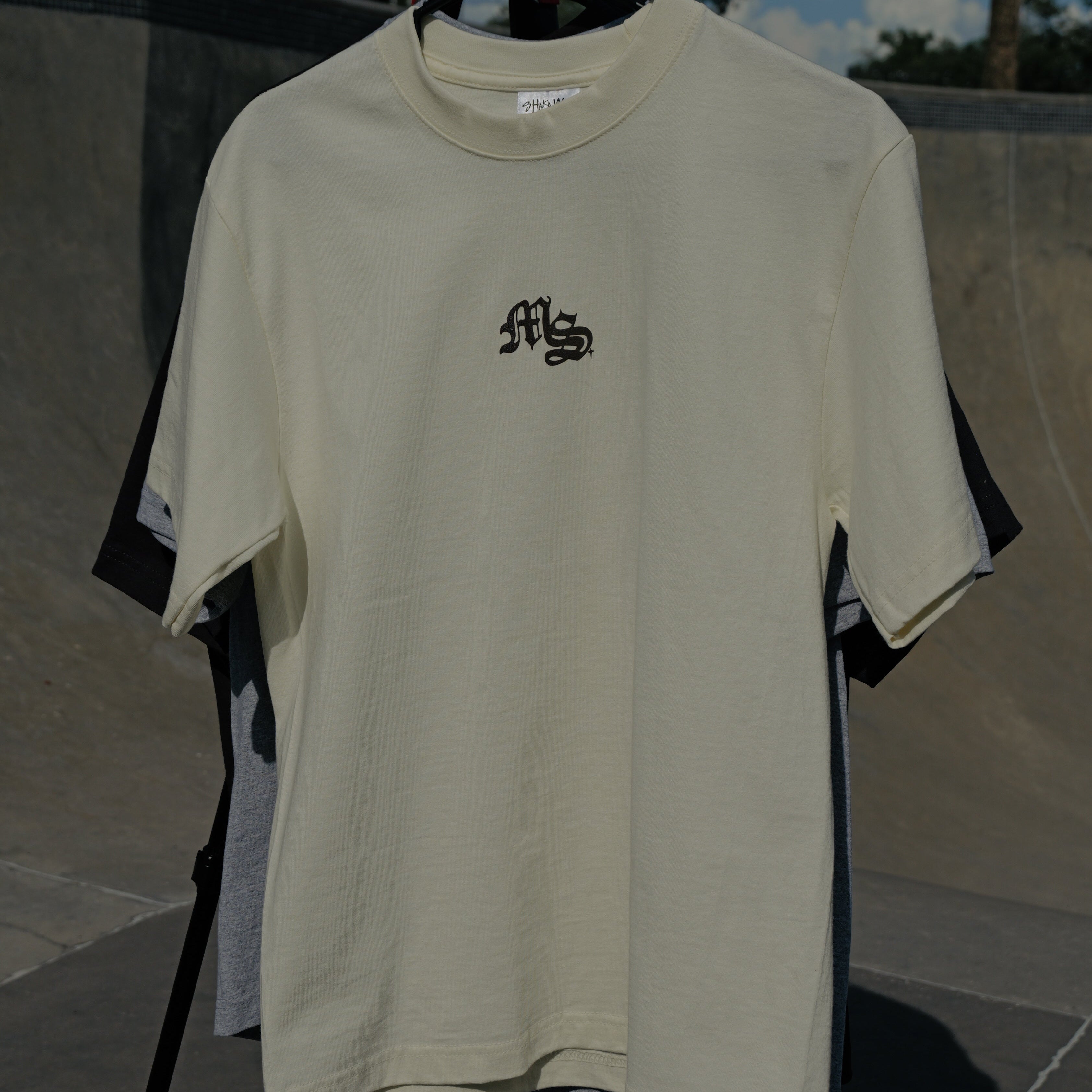 Beige t-shirt with a logo on a hanger against a skate park background